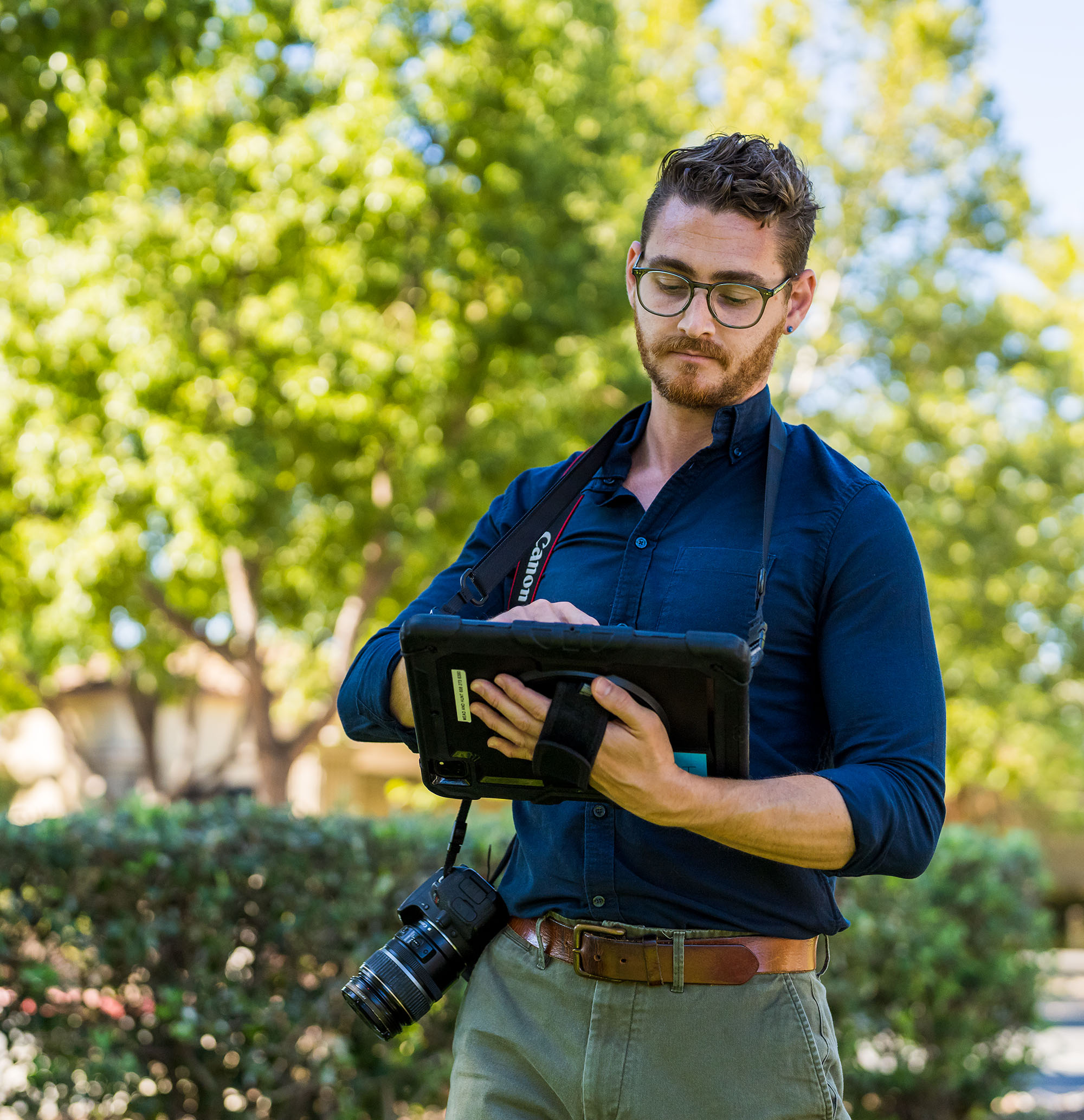 A Mead & Hunt Employee records data on a device while standing amongst trees during the day